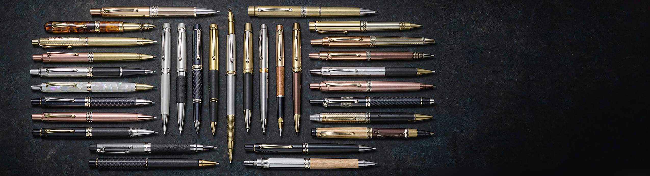 Metal pens in brass, stainless steel, gunmetal and gold finishes laid out side by side